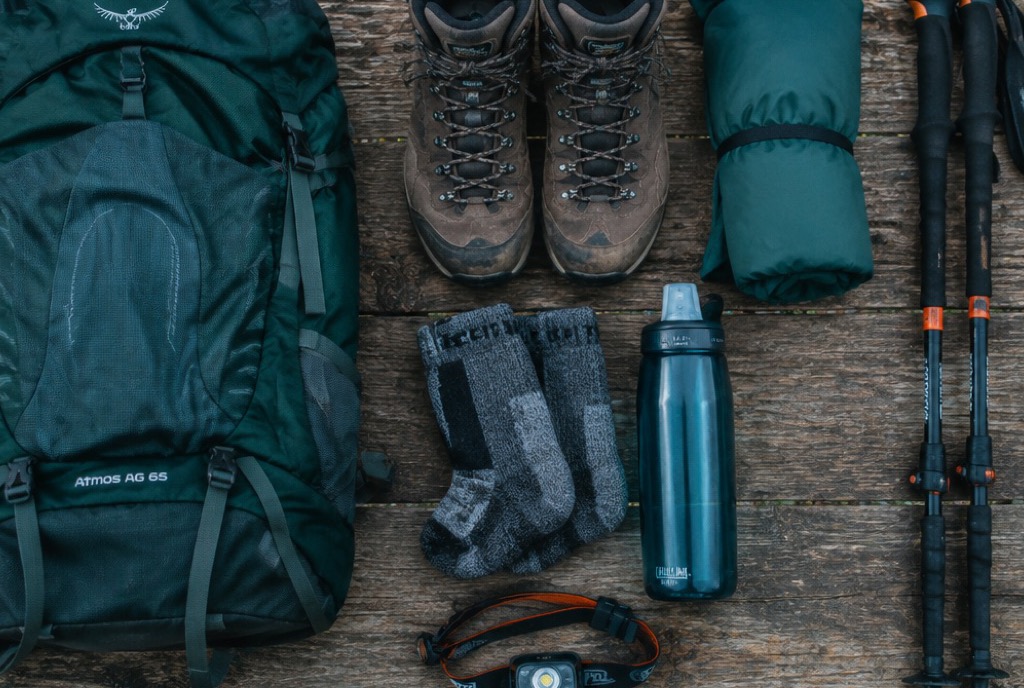 Trekking-Grundausstattung mit Wanderschuhen, Rucksack, Regenjacke und Zubehör auf einem Holztisch